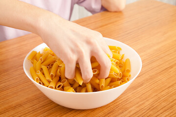 Uncooked raw healthy and pasta macaroni hand held by a Caucasian man, on wooden table in porcelain plate