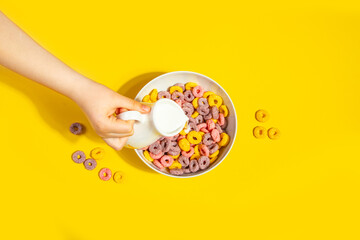 Bowl of colorful cereal corn rings on yellow table. Breakfast concept.