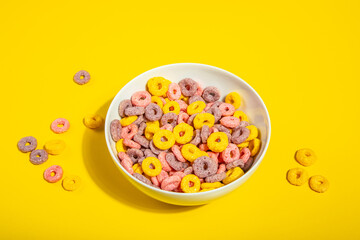 Bowl of colorful cereal corn rings on yellow table. Breakfast concept.