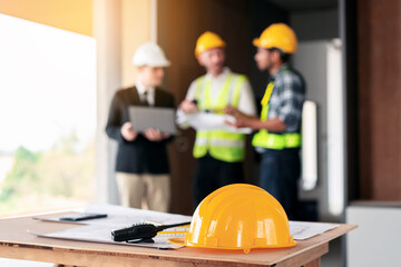 Three men wearing hard hats are standing around a table with blueprints