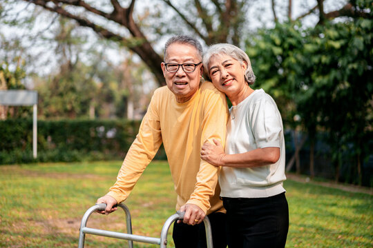 A couple of older people are standing in a grassy area, one of them holding a walker