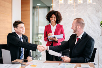 Three people in suits shaking hands in a conference room