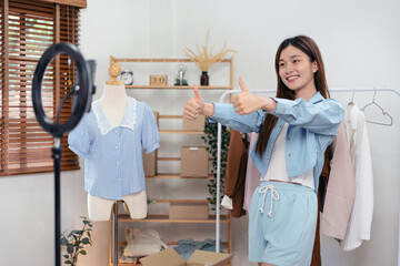 Female online seller is using smartphone to broadcast live on Vlog while making thumbs up for introduce