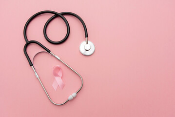 Breast cancer awareness pink ribbon and stethoscope on pink background with copy space