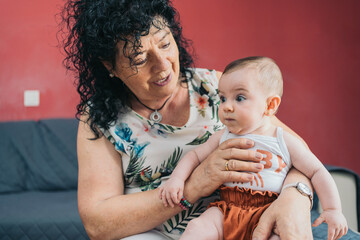 Grandmother holding baby girl on lap smiling at home. Grandmother holding her baby granddaughter on her lap, smiling at her with love