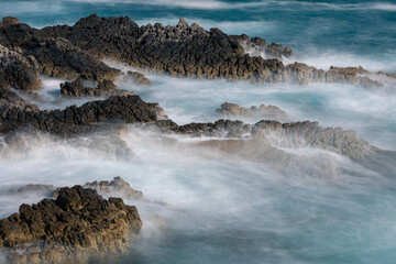Long exposure shoot of sea waves crashing on seashore and rocks seascape.