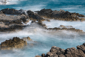 Long exposure shoot of sea waves crashing on seashore and rocks seascape.
