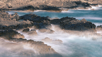 Long exposure shoot of sea waves crashing on seashore and rocks seascape.