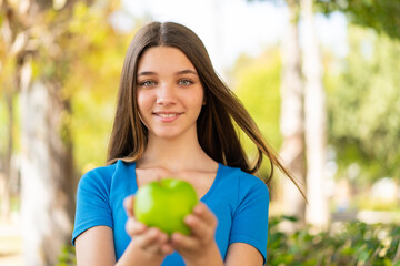 Teenager girl at outdoors holding an apple with happy expression