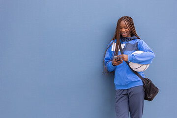 Horizontal photo young woman in blue sportswear with basketball using smartphone. Sport concept.
