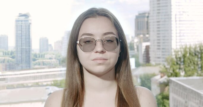 Girl wearing glasses with photochromic lenses. The lenses adjust to changing light conditions, becoming darker in the sun after being transparent indoors. Portrait. Urban city landscape background