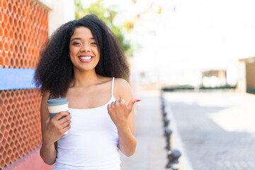 Young African American woman holding a take away coffee at outdoors pointing to the side to present a product