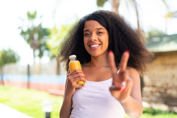 Young African American woman holding an orange juice at outdoors smiling and showing victory sign