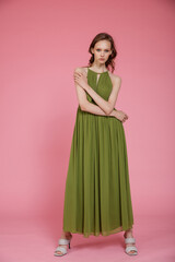 High fashion photo of a beautiful elegant young skinny woman in pretty long green dress posing on pink background. Slim figure.