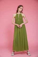 Fototapeta premium High fashion photo of a beautiful elegant young skinny woman in pretty long green dress posing on pink background. Slim figure.