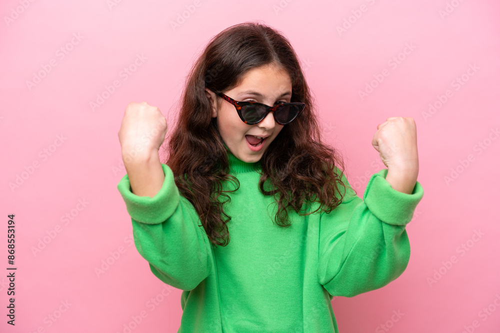 Wall mural little caucasian girl wearing sunglasses isolated on pink background celebrating a victory