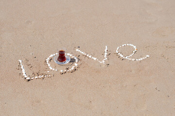 inscription love on the wet sand of the sea beach in Turkey lined with white shells, with a cup of Turkish Armudu tea, the inscription on the sand,love message, declaration of love