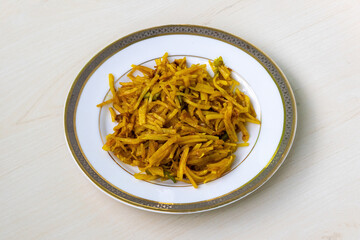 Tasty aloo bhaji or fried grated potato in a white plate on wooden background. Authentic bengali food which is thin potato slices deep fried using turmeric and some mild spices.