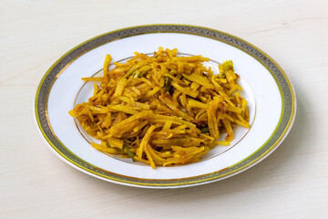 Delicious aloo bhaji or fried grated potato in a white plate on wooden background. Authentic bengali food which is thin potato slices deep fried using turmeric and some mild spices.