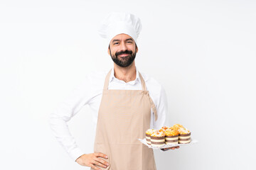 Young man holding muffin cake over isolated white background posing with arms at hip and smiling