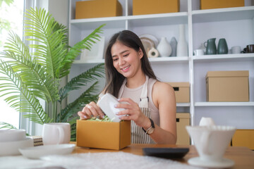 Young woman pottery store owner working at her shop packing the products for delivery to customer. E-commerce concept.