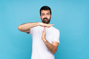 Young man with beard  over isolated blue background making time out gesture