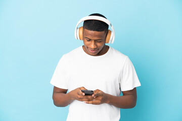 Young latin man isolated on blue background listening music and looking to mobile