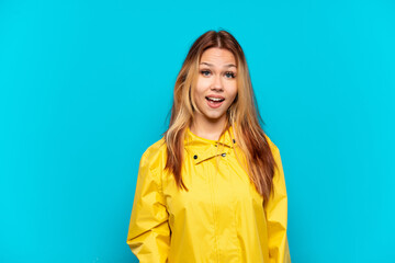 Teenager girl wearing a rainproof coat over isolated blue background with surprise facial expression