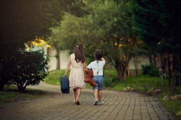 Obraz premium Adventure, back of children and suitcase on path for play, fantasy and walking away with teddy bear. Girl, young boy and together on driveway for bonding, sibling love and outdoor activity at home