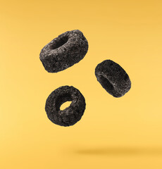 Delicious crunchy black cereal rings falling in the air isolated on yellow background. High...