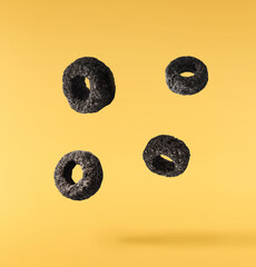 Delicious crunchy black cereal rings falling in the air isolated on yellow background. High...