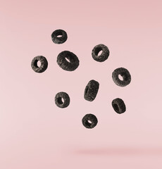 Delicious crunchy black cereal rings falling in the air isolated on pink background. High...