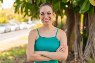 Young pretty woman with glasses at outdoors keeping the arms crossed in frontal position