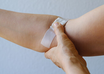 Closely removed white plaster, bandage on the bend of the elbow. The woman presses her thumb against the injection site and bends her arm to stop the bleeding. Blood donation, annual check-up concept.