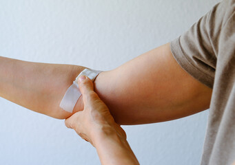 Closely removed white plaster, bandage on the bend of the elbow. The woman presses her thumb against the injection site and bends her arm to stop the bleeding. Blood donation, annual check-up concept.