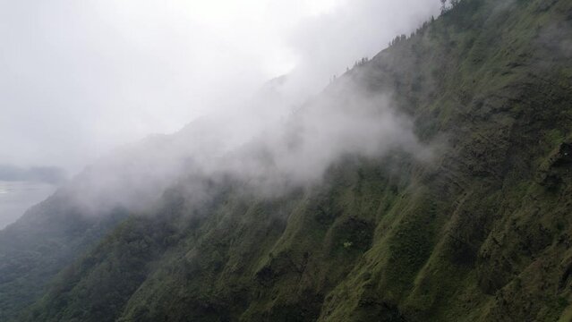 As camera flies out from trekking path and glides through ethereal embrace of clouds, spectacular panorama unfolds before our eyes. Emerging from fog, we see steep slope of Mount Abang