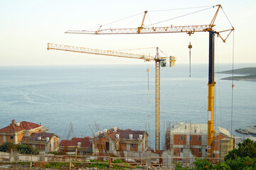 Construction of residential buildings on the coast: top view of unfinished houses made of concrete and brick, tower cranes and the Adriatic Sea. Investments in real estate in Montenegro.