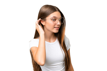 Teenager caucasian girl over isolated background listening to something by putting hand on the ear