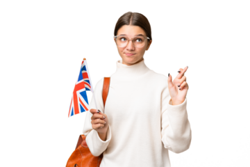 Teenager student caucasian girl holding an United Kingdom flag over isolated background with fingers crossing and wishing the best