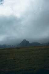 Moody view of a rocky mountain peak covered in fog and clouds with sunlight peeking trough the clouds from above.