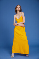 High fashion photo of a beautiful skinny young woman in pretty long yellow dress posing on blue background. Slim figure.