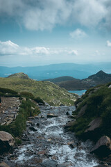 Small river at high altitude coming from one of the Rila lakes to another one below. Background. Cloudscape.