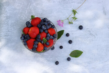 Beautiful summer still life with seasonal fruit. Strawberries and blueberries in a glass bowl on a gray background with space for text. Eating fresh concept. Vitamins and antioxidants