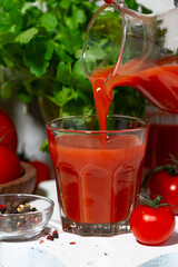 fresh tomato juice is poured into a glass from a jug