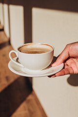 White cup of morning tasty coffee in the hand, sunny day