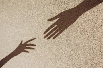 Shadows of hands reaching each other on the wall. Abstract blurred effect with space for text.