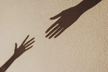 Shadows of hands reaching each other on the wall. Abstract blurred effect with space for text.