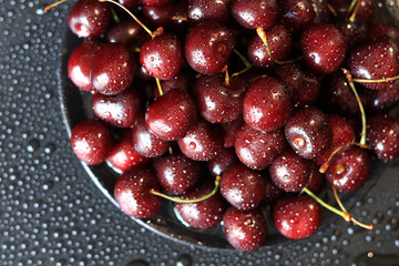 Cherry berries on a black background, close-up. Wet sweet ripe cherries. Dark red cherries with green stems covered with fine splashes of water. Summer berries, vitamins. Background