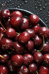 Cherry berries on a black background, close-up. Wet sweet ripe cherries. Dark red cherries with green stems covered with fine splashes of water. Summer berries, vitamins. Background