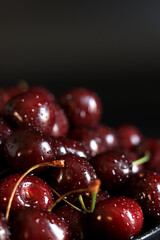 Cherries in a black plate on a dark wet background, close-up. Wet sweet ripe cherries. Dark red cherries with green stems covered with fine splashes of water. Summer berries, vitamins
